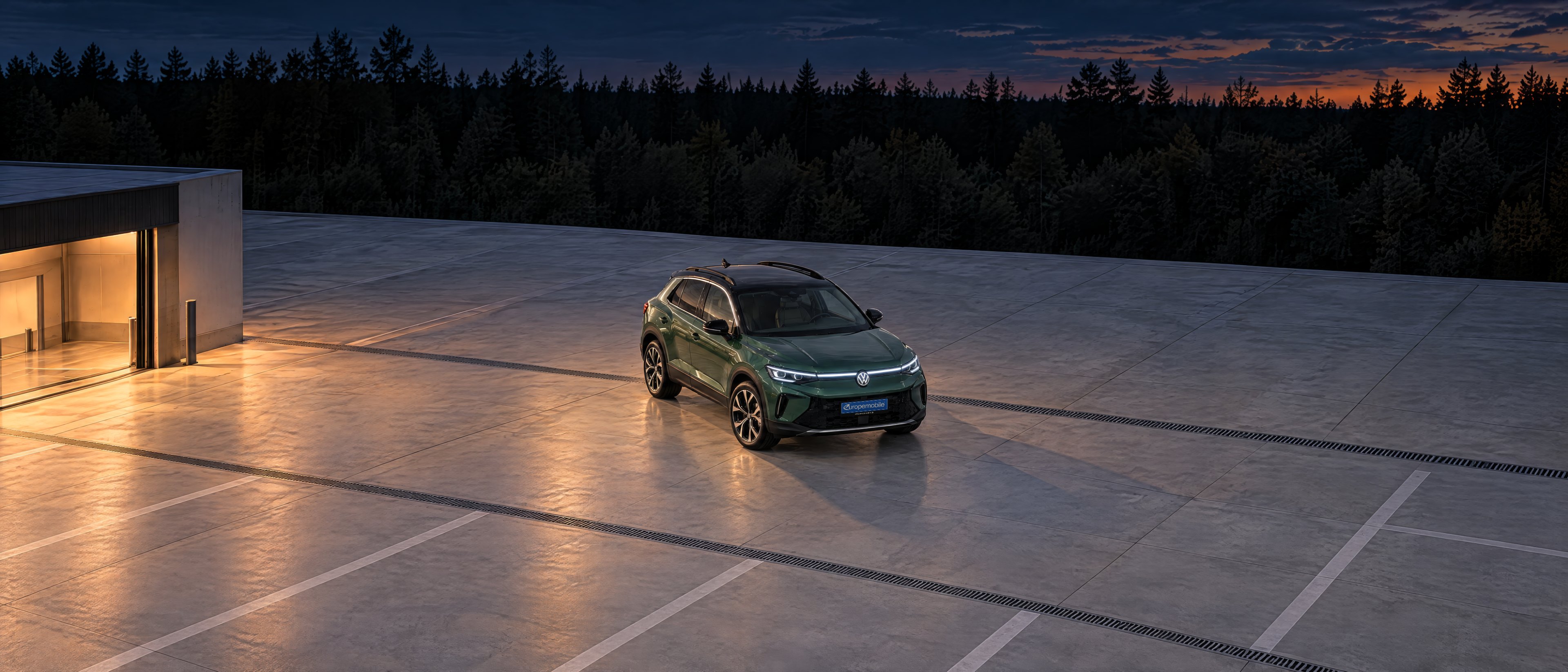 Luftbild eines Prüfstellen-Hofs am Abend mit einem dunkelgrünen VW T-Roc, links die beleuchtete Prüfhalle