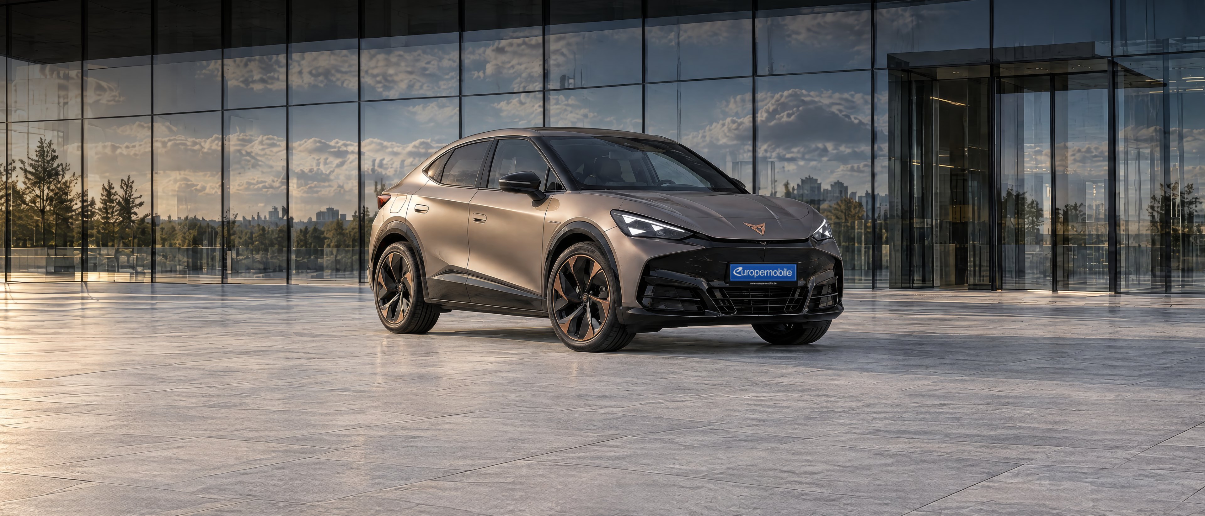 Cupra Tavascan in Bronze matt vor der Glasfassade eines modernen Bürogebäudes bei Tageslicht