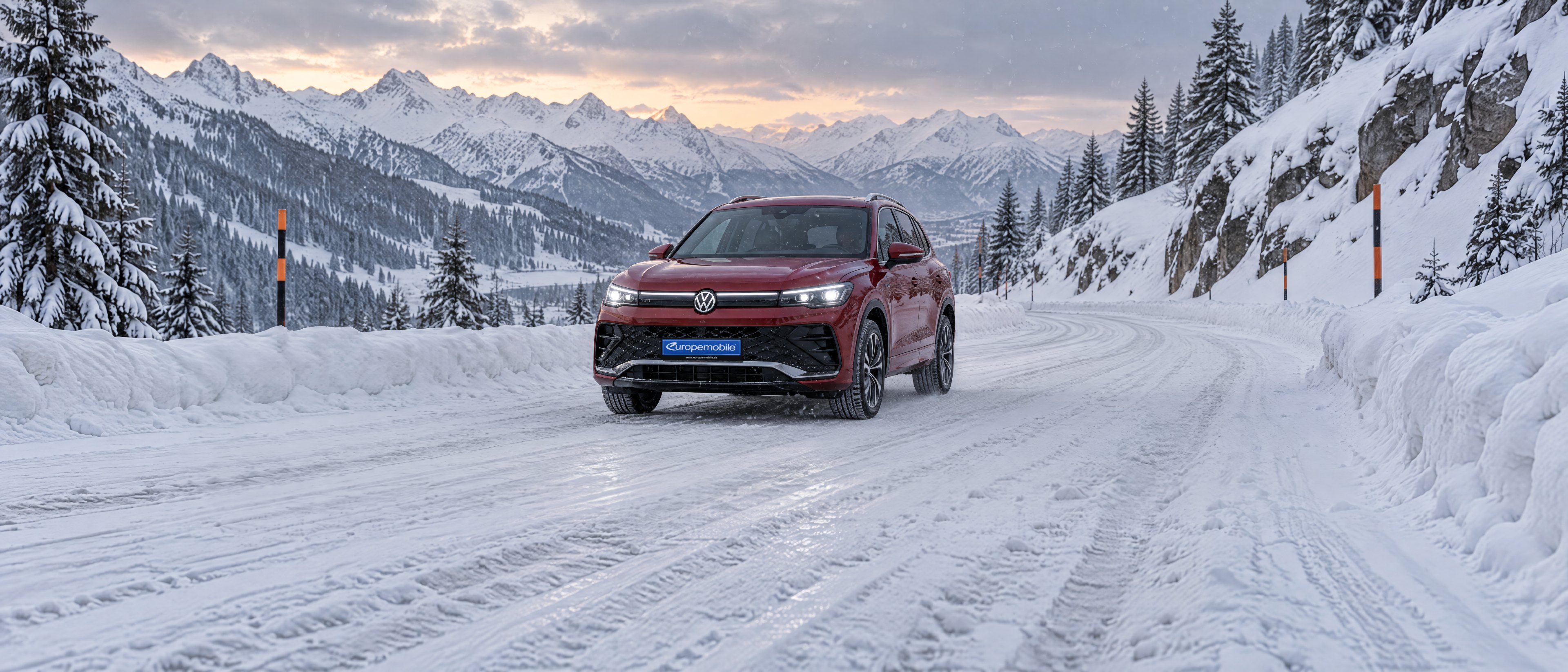 VW Tiguan 2026 in Rot auf einer verschneiten Alpen-Passstraße bei leichtem Schneefall