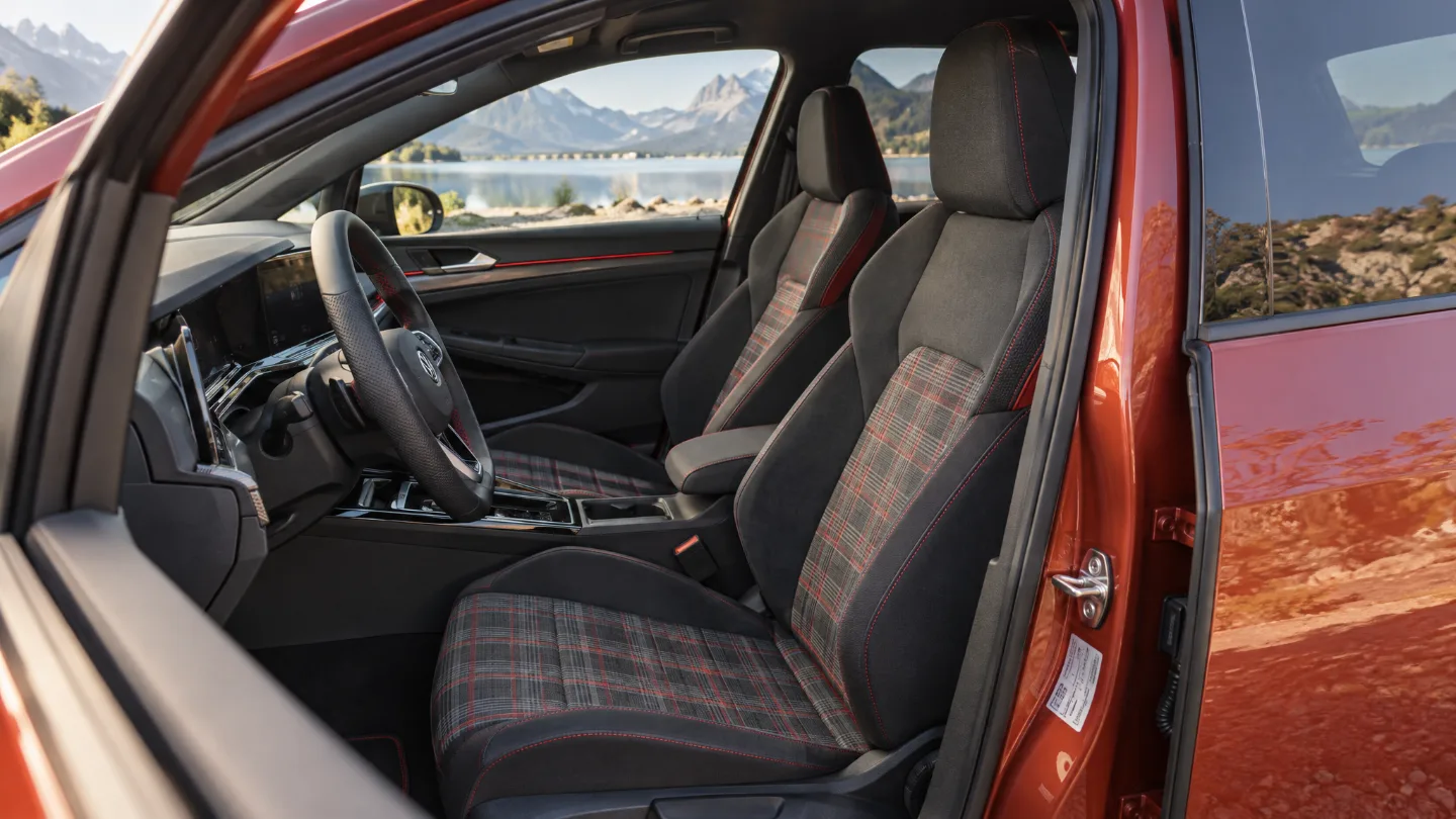 Sportsitz mit kariertem GTI-Stoffmuster und Sportlenkrad in einem aktuellen VW Golf GTI, durch die Scheiben ein Bergsee