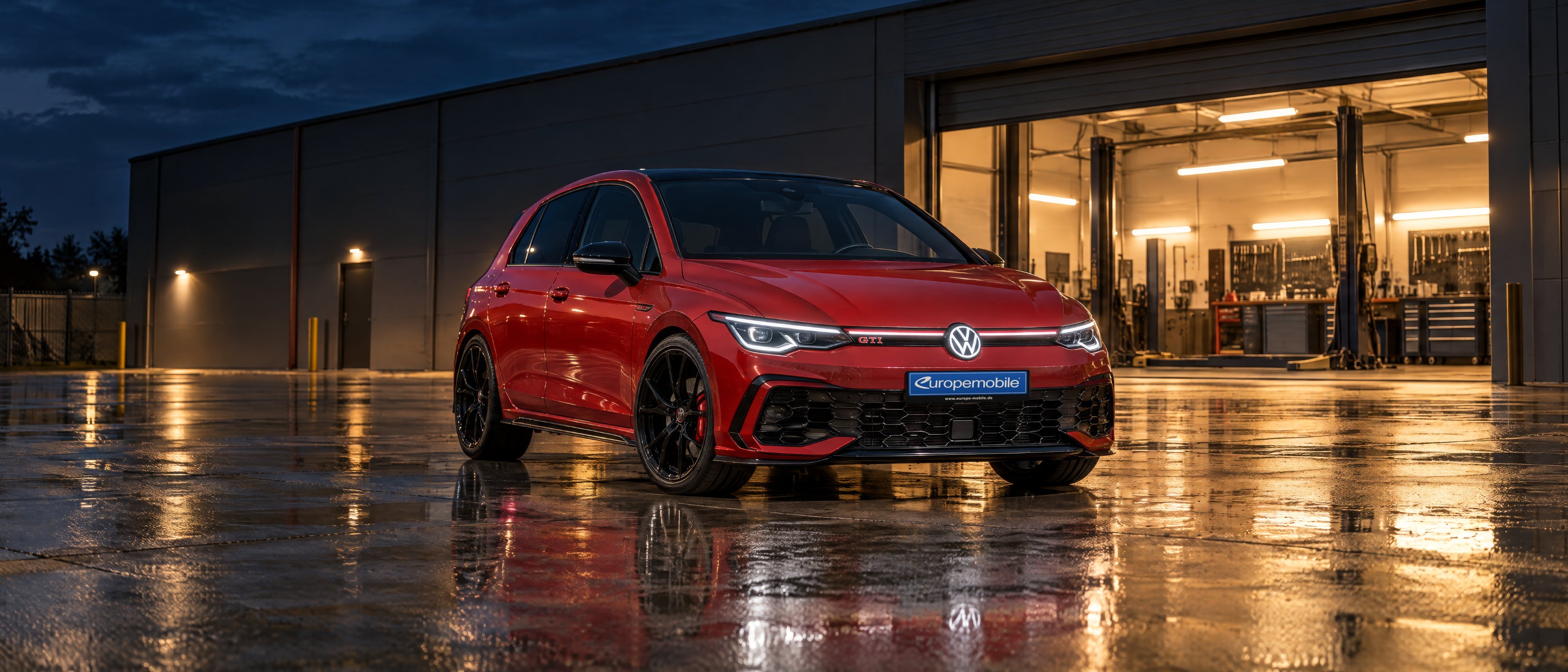 VW Golf GTI Edition 50 in Tornadorot mit schwarzem Dach vor einer beleuchteten Werkstatt bei Nacht